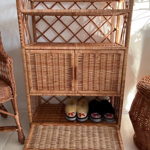 May include: A wicker cabinet with two doors, two shelves, and a pull-out drawer. The cabinet is made of natural woven wicker and has a light brown color.