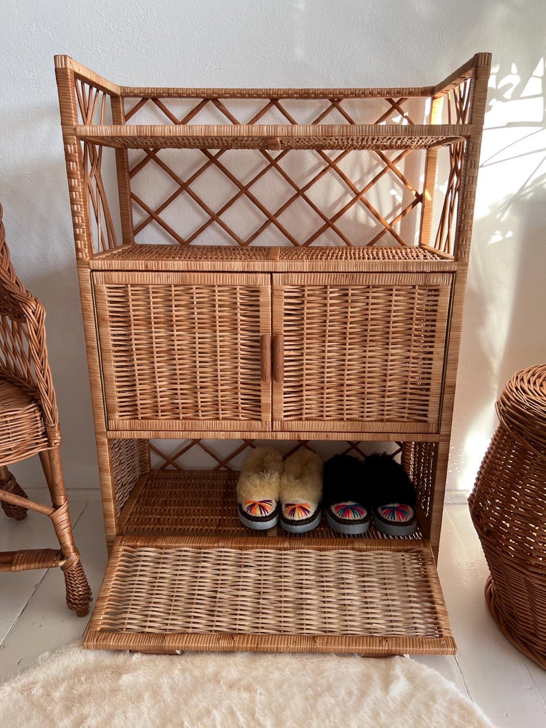 May include: A wicker cabinet with two doors, two shelves, and a pull-out drawer. The cabinet is made of natural woven wicker and has a light brown color.