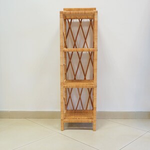 May include: A natural woven wicker shelf unit with three shelves. The shelf unit is made of light brown wicker and has a diamond pattern on the sides.
