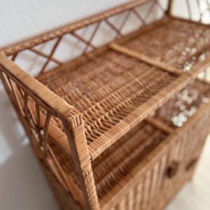 May include: A natural woven wicker shelf unit with two open shelves and a cabinet with a door. The cabinet has a small knob handle.