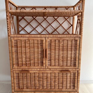 May include: A wicker cabinet with two doors and two drawers. The cabinet has a woven design and a natural wood finish.