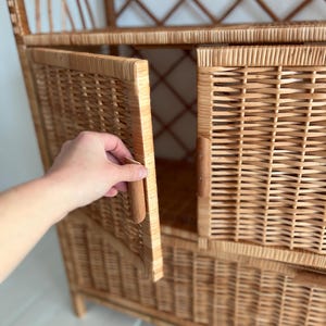 May include: A wicker cabinet with a door that is open. The cabinet has a woven design and a natural wood color.