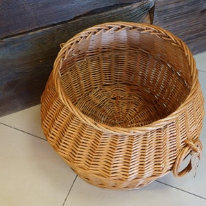 Puede incluir: Una cesta grande, redonda y tejida de mimbre de color marr&oacute;n natural. La cesta tiene una abertura ancha y un asa a cada lado.