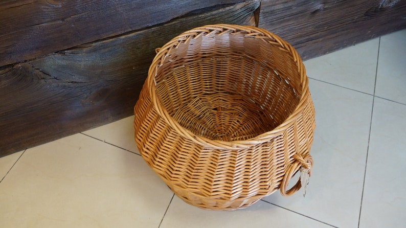 Puede incluir: Una cesta grande, redonda y tejida de mimbre de color marr&oacute;n natural. La cesta tiene una abertura ancha y un asa a cada lado.