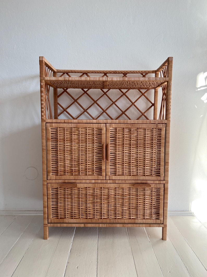 May include: A natural woven wicker cabinet with two doors and two drawers. The cabinet has two shelves on top and a lattice design on the front.