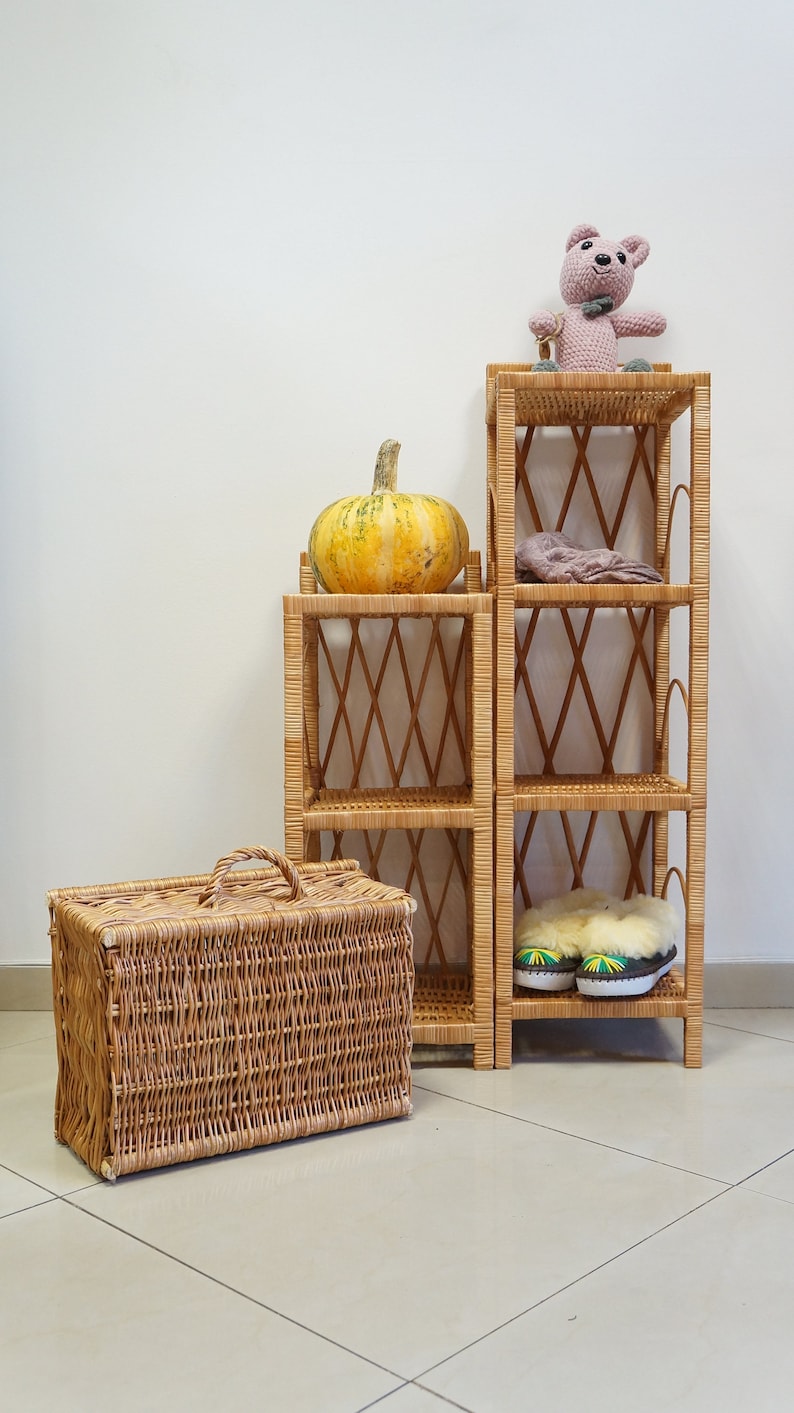 May include: Two wicker shelves with a pumpkin on the top shelf, a stuffed animal on the top shelf of the taller shelf, and a pair of slippers on the bottom shelf of the taller shelf.