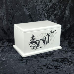 May include: White wooden cremation urn featuring a black and white engraved image of a waterfall in a forest setting.