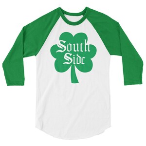 May include: A white and green baseball t-shirt with a shamrock design and the text "South Side" in a white font.