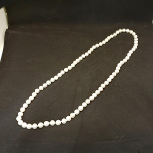May include: A strand of white pearl beads on a black background.