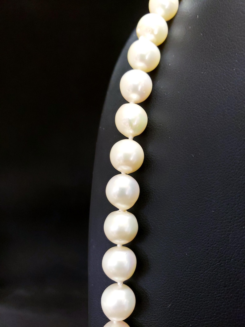 May include: A strand of white pearls on a black display stand. The pearls are round and smooth, and they are strung together on a thin, white thread.