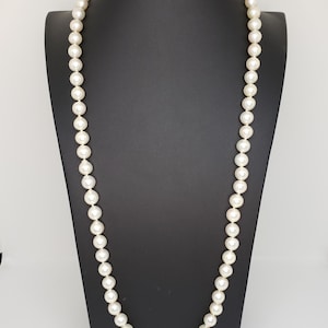 May include: A long strand of white pearls on a black display stand. The pearls are round and smooth.