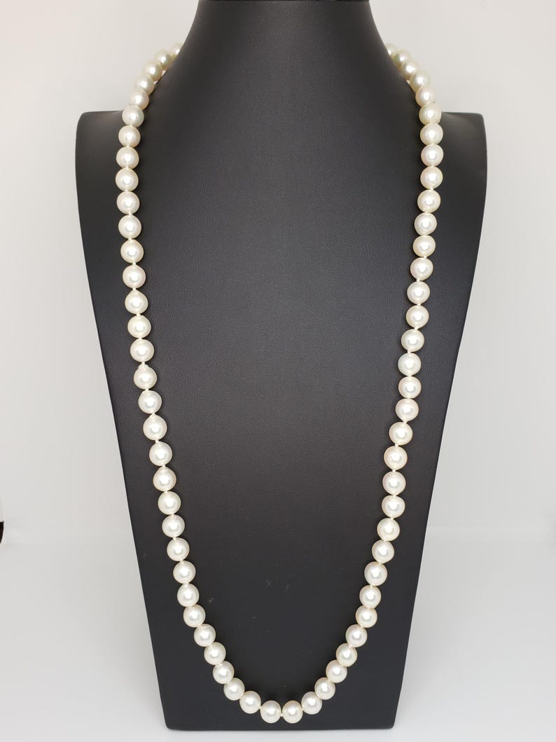 May include: A long strand of white pearls on a black display stand. The pearls are round and smooth.