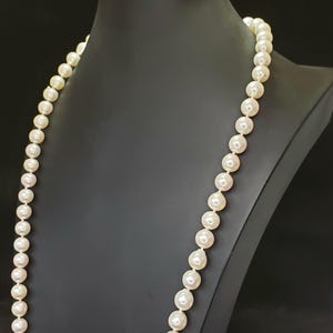 May include: A long strand of white pearls on a black display stand. The pearls are round and smooth, and the necklace is approximately 76 cm long.