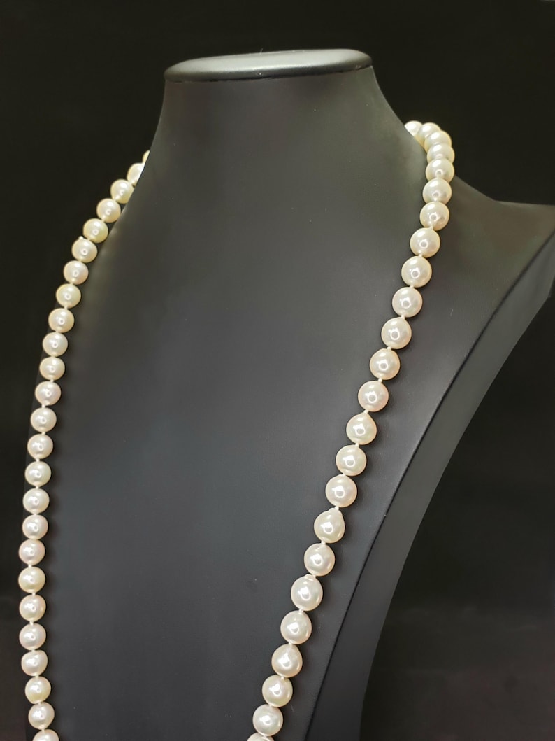 May include: A long strand of white pearls on a black display stand. The pearls are round and smooth, and the necklace is approximately 76 cm long.