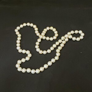May include: A set of white pearl necklaces, one long and one shorter, on a black background.