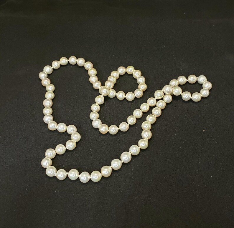 May include: A set of white pearl necklaces, one long and one shorter, on a black background.