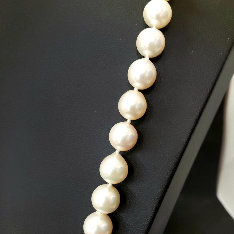 May include: A strand of white pearls on a black background. The pearls are round and smooth, and they are strung together on a thin thread.