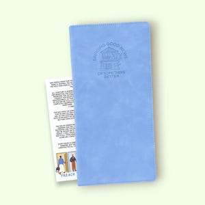 Könnte beinhalten: Ein hellblaues Notizbuch mit dem geprägten Text "Bringing Good News of Something Better". Eine kleine Karte mit Text und Illustrationen befindet sich neben dem Notizbuch. Das Wort "PREACH" ist auf der Karte zu sehen.