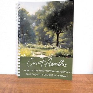 Può includere: Un taccuino con rilegatura a spirale che presenta un dipinto paesaggistico di alberi e fiori sulla copertina. Il testo recita 20-27 Circuit Assemblies, Happy is the one trusting in Jehovah e Find exquisite delight in Jehovah su sfondo verde.