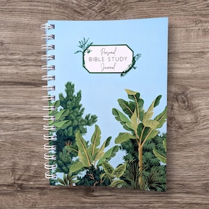 Peut inclure: Un journal à spirales avec une couverture bleu clair ornée d'un motif de feuillage tropical. La couverture porte l'inscription "Personal BIBLE STUDY Journal" dans une police décorative. Les pages du journal sont maintenues par une spirale blanche.