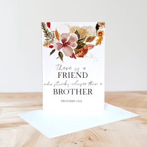 Könnte beinhalten: Eine weiße Grußkarte mit einem Aquarell-Blumenarrangement in Rosa-, Orange- und Goldtönen am oberen Rand. Der Text lautet: There is a FRIEND who sticks closer than a BROTHER -PROVERBS 18:24. Die Karte wird zusammen mit einem Umschlag präsentiert.