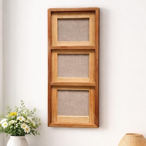 May include: A vertical wooden picture frame with three openings. The frame is made of light brown wood and has a natural finish. Each opening has a neutral-colored backing. The frame is mounted on a white wall.