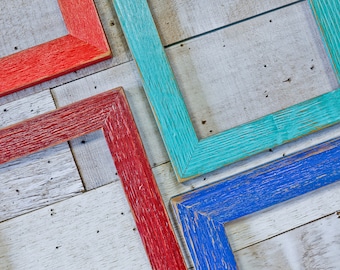 May include: Close-up of four colorful wooden picture frames. The frames are painted in red, turquoise, and blue, with a distressed finish. The frames are arranged on a light-colored, weathered wooden surface.