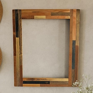 May include: Rectangular wooden picture frame with a patchwork design. The frame is made of various shades of brown wood, with accents of black and gold. The frame is empty, ready for a photo or artwork. The frame is a decorative home decor item.