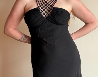 May include: Black formal dress with a strapless bodice and crisscross straps. The dress features a ruched bust and a flowing skirt with a subtle flare at the hem. The dress is made of a soft, flowing fabric.