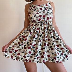 May include: A white sleeveless dress with a floral print featuring red, yellow, and green flowers. The dress has a fitted bodice and a flowing skirt.