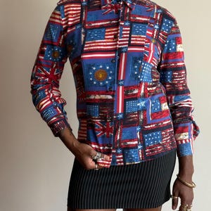May include: A long-sleeved button-down shirt featuring a patchwork design of American and British flags in red, white, and blue. The shirt is paired with a black and white pinstripe mini skirt.