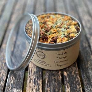May include: A silver tin filled with dried herbs and orange peel for simmering potpourri. The label reads "Herb & Orange Simmering Potpourri" and "Hand Made, Gladewater, TX 75647, sweetrootcoaching.com".