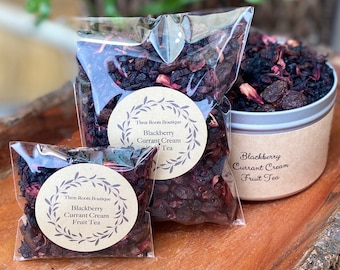 May include: Two clear plastic bags filled with dried fruit and herbs for tea. The bags have brown paper labels with the text "Three Roots Boutique Blackberry Currant Cream Fruit Tea".