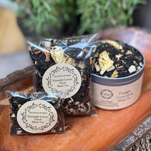 May include: Three bags of loose leaf tea, one in a tin container, all labeled "Pineapple Lemon Decaf Black Tea" by Three Roots Boutique.