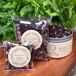May include: Three Roots Boutique Strawberry Fruit Tea in a clear plastic bag with a brown label. The tea is also available in a silver tin with a brown label. The label says "Hand Made, Adewater TX 75647, threrootscoaching.com".
