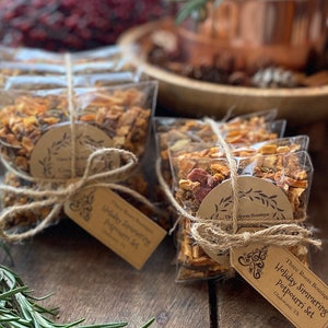 Puede incluir: Bolsas transparentes de celof&aacute;n llenas de popurr&iacute; seco, atadas con hilo y una etiqueta de papel marr&oacute;n. La etiqueta dice "Holiday Simmering Potpourri Set". El popurr&iacute; incluye frutas secas y especias.