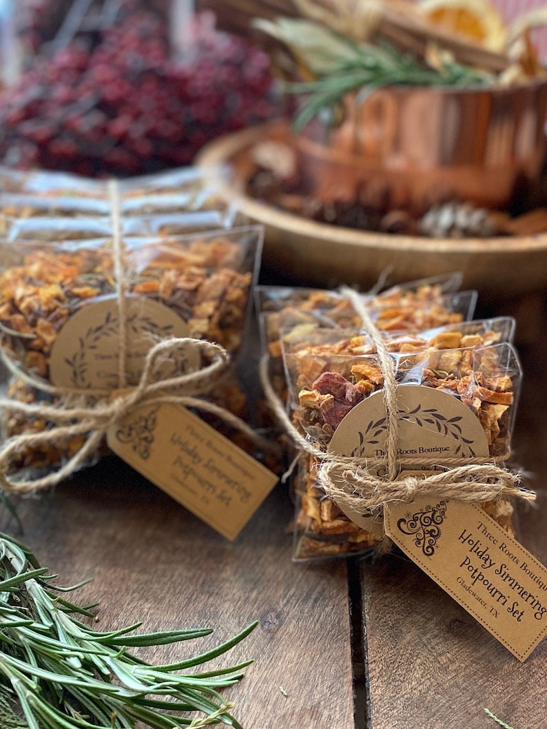 Puede incluir: Bolsas transparentes de celof&aacute;n llenas de popurr&iacute; seco, atadas con hilo y una etiqueta de papel marr&oacute;n. La etiqueta dice "Holiday Simmering Potpourri Set". El popurr&iacute; incluye frutas secas y especias.