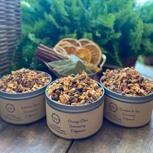 May include: Three metal tins of simmering potpourri with labels: "Autumn Spice Simmering Potpourri", "Orange Chai Simmering Potpourri", and "Comfort & Joy Simmering Potpourri".