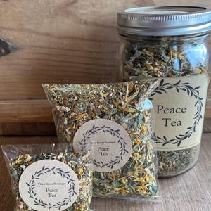 May include: Three sizes of loose leaf tea blends in clear plastic bags with brown paper labels. The labels have a wreath design and the text "Three Roots Boutique Peace Tea".