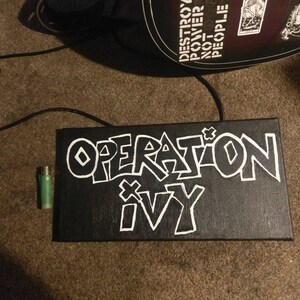 May include: A black canvas with white paint, featuring the words "Operation Ivy" in a graffiti style font.