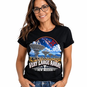 May include: A black t-shirt featuring a graphic print of the Very Large Array radio telescope in New Mexico. The design includes multiple satellite dishes in a desert landscape under a starry sky, a red Zia symbol, and the text "VERY LARGE ARRAY NEW MEXICO".