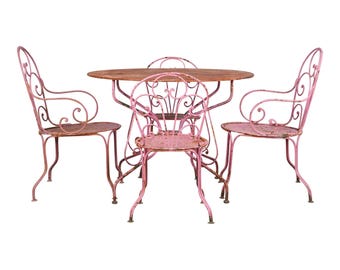 May include: A pink metal patio set with a round table and four chairs. The chairs have ornate, scrolled backs and arms.