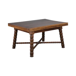 May include: A dark brown wooden table with a rectangular top and a unique, intricate design on the legs. The table has a drop-leaf extension on one side.