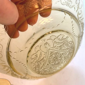 May include: A yellow glass bowl with a floral design. The bowl has a gold rim and a raised design in the center.