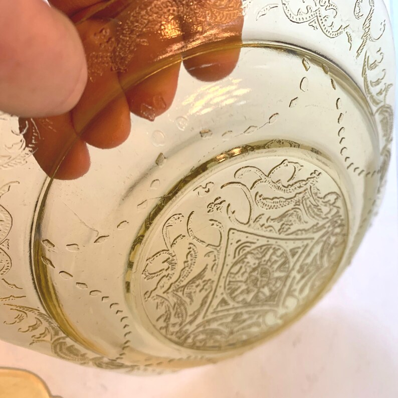May include: A yellow glass bowl with a floral design. The bowl has a gold rim and a raised design in the center.