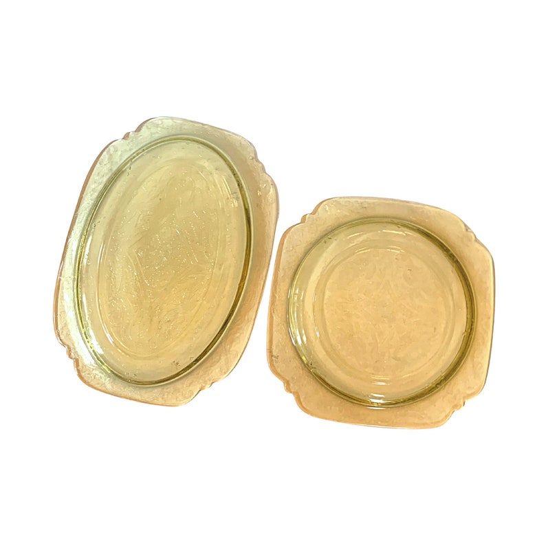 May include: Two yellow glass dishes, one oval and one round, with a decorative pattern. The dishes are made of clear glass with a yellow tint.