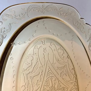 May include: A vintage oval glass serving dish with a delicate etched floral design. The dish has a gold rim and a creamy white color.
