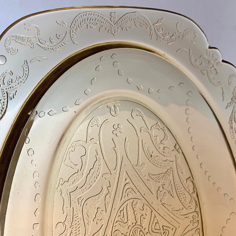 May include: A vintage oval glass serving dish with a delicate etched floral design. The dish has a gold rim and a creamy white color.