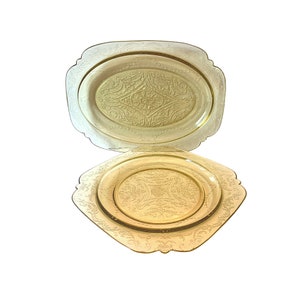 May include: Two vintage yellow glass plates with an intricate etched design. The larger plate is oval shaped and the smaller plate is square.