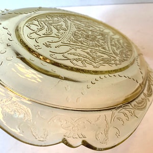 May include: A yellow glass serving dish with an intricate floral design. The dish has a scalloped edge and a raised center.